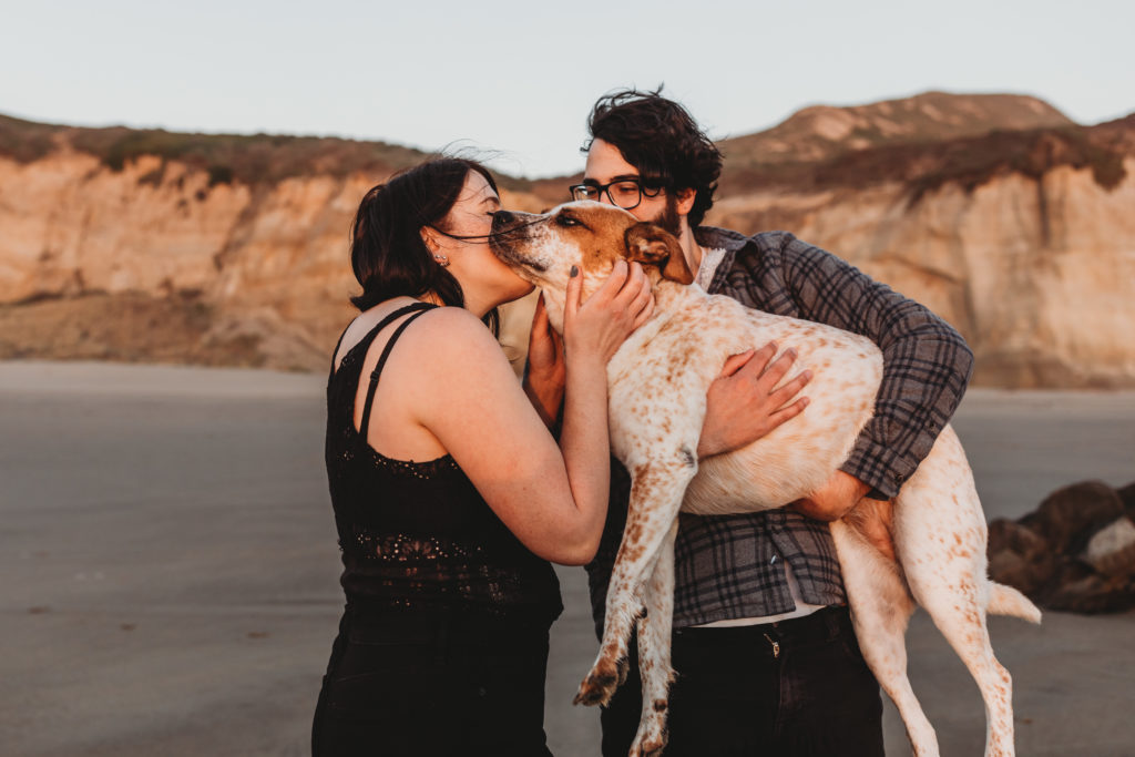 couple at beach with dog kissing dog