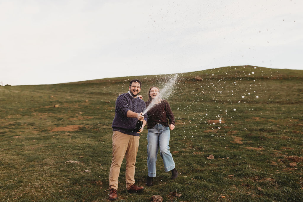 couple popping champagne during engagement photoshoot at preserve