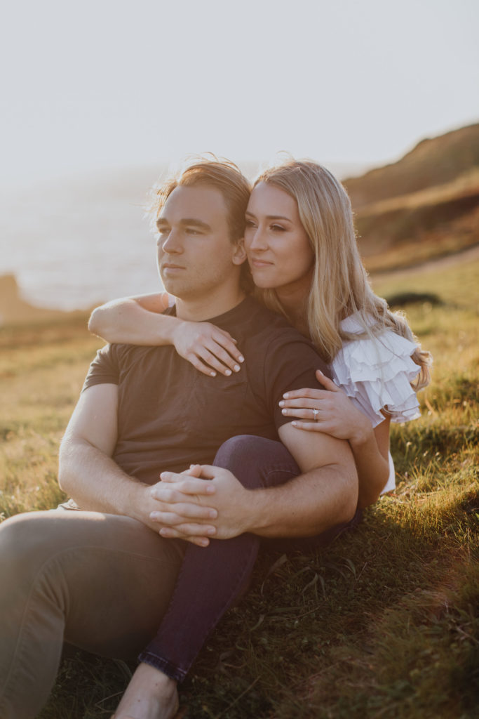 man and woman sitting on a hill for engagement photos