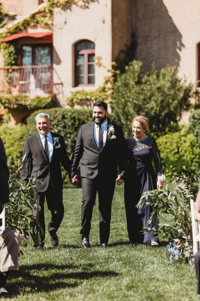 groom walking with parents down isle at outdoor ceremony